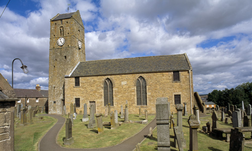 A church building with a clock on the tower and two tall large windows, set in a graveyard 
