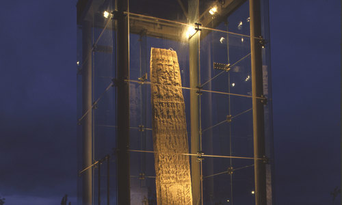 A very tall standing stone is encased by a glas enclosure and is lit up during the night