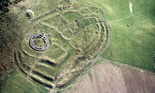 An aerial shot showing the foundations of a broch surrounded by a network of large ramparts and ditches