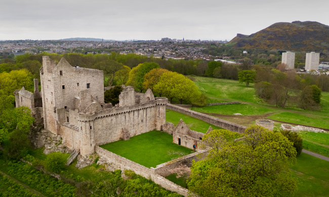 Aerial view of the stone buildings of Craigmillar Castle with the city of Edinburgh in the background.