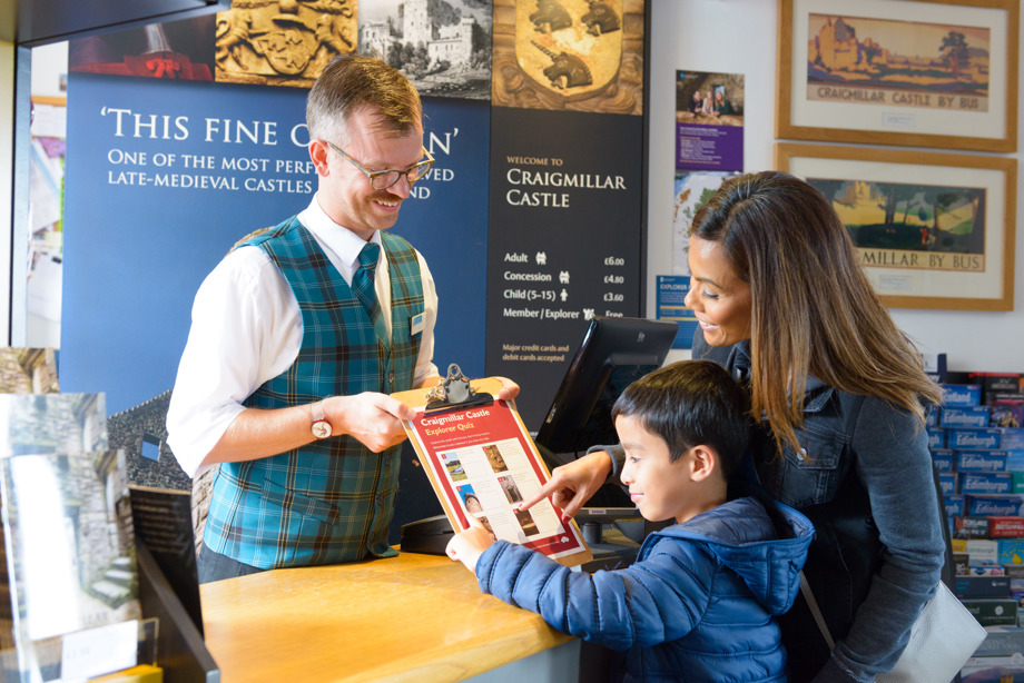 A Historic Scotland member of staff is handing over a quiz sheet to a young boy and his mother.