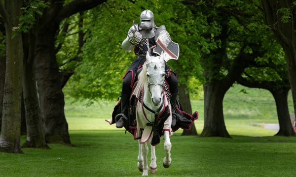 A knight in costume rides towards the camera on a horse