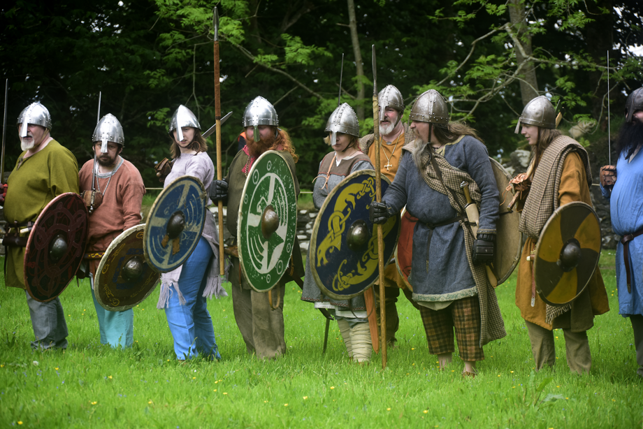 A group of Viking reenactors with helmets, spears and shield in different colours and designs are in a battle line.