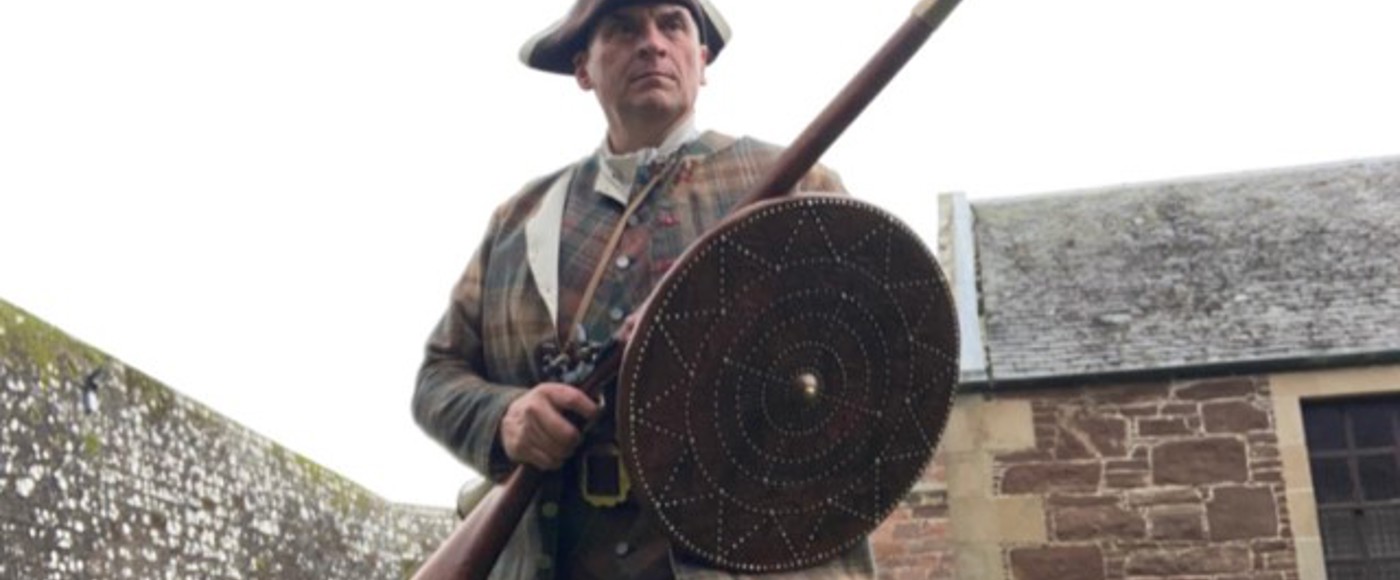 A reenactor dressed as Sir Rodrick Chisholm, holding a rifle and shield