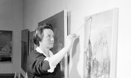 A woman holding a paintbrush and looking at her canvas