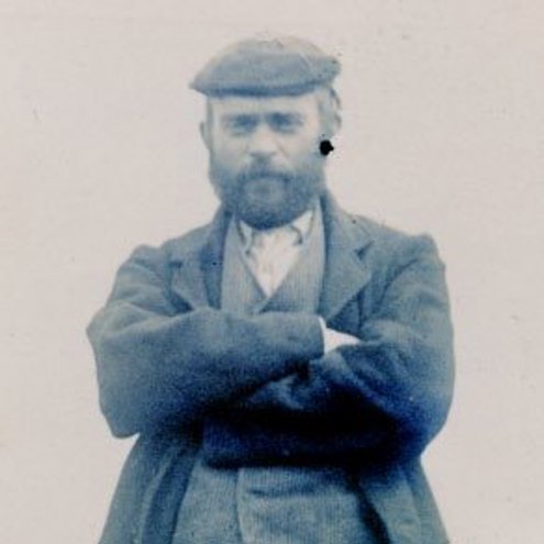 Black and white photograph taken in 1901 of Adam Christie. He is wearing a waistcoat and outer jacket, with a flat cap. His arms are folded and he is looking into the camera with a stern expression on his bearded face.