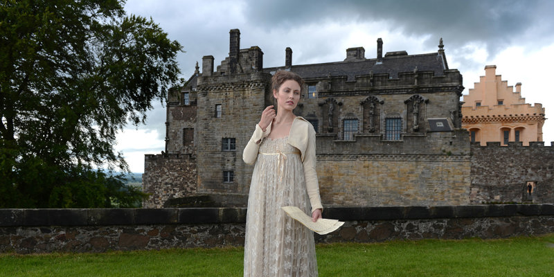 A lady wearing a long cream dress bolero jacket holding letters with Stirling Castle