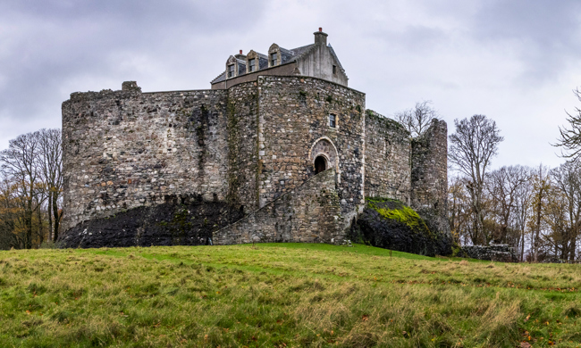 Dunstaffnage Castle with it's high stone walls and staircase up to the entrance, in a grassy landscape with trees.