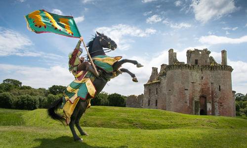 A knight raising a flag on a horse with Caerlaverock Castle in the background 