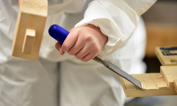 A person using a mallet and a chisel, working on some wood 
